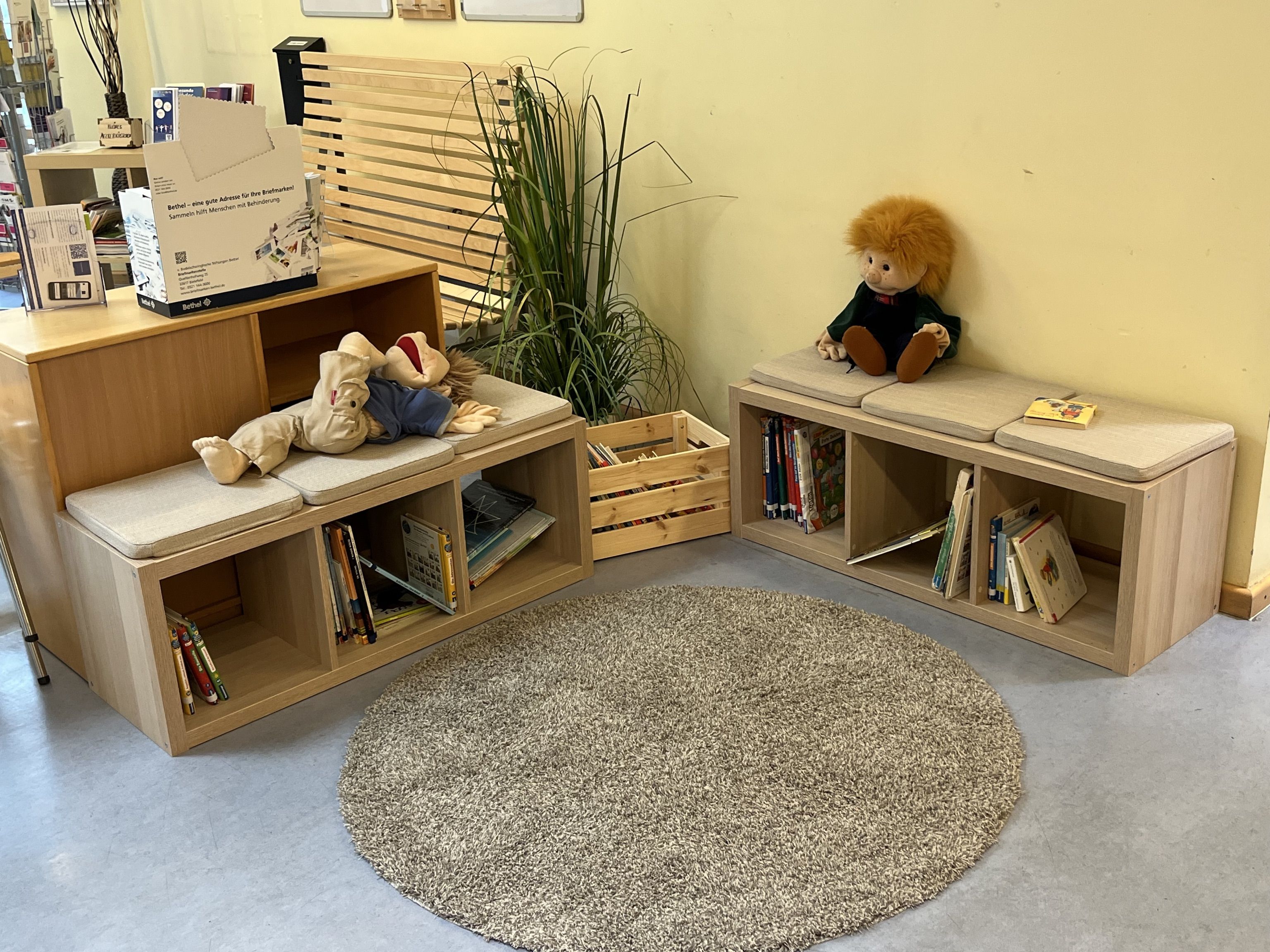 Abgebildet ist unsere gemütliche Leseecke mit aktuellen Büchern und einem flauschigen, runden, grauen Teppich auf dem Boden.